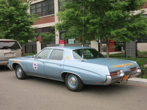 Light blue 1970s police sedan with orange POLICE lettering, rear view