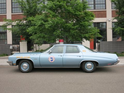 Light blue 1970s police sedan profile view with orange lettering and seal