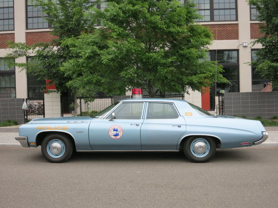 Light blue 1970s police sedan profile view with orange lettering and seal