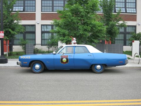 Blue and white 1970s Plymouth police sedan profile with door shield