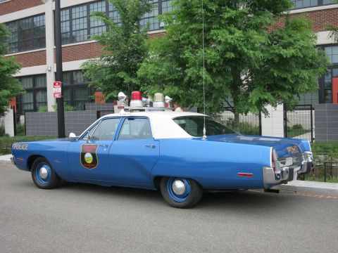 Blue and white 1970s police sedan rear three-quarter view with shield
