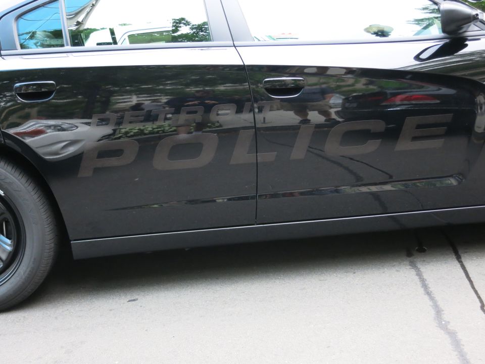 Close-up of a black Detroit Police car door with subdued gray POLICE lettering
