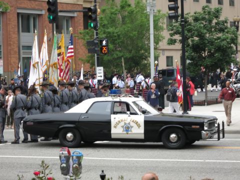 Black and white CHP sedan passing a uniformed honor guard with flags