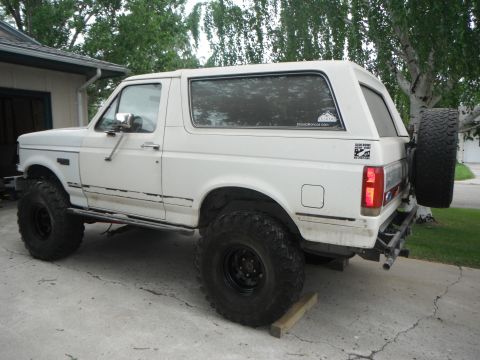 1990 Ford Bronco - This white SUV features oversized tires and a rear-mounted spare, suggesting off-road modifications.