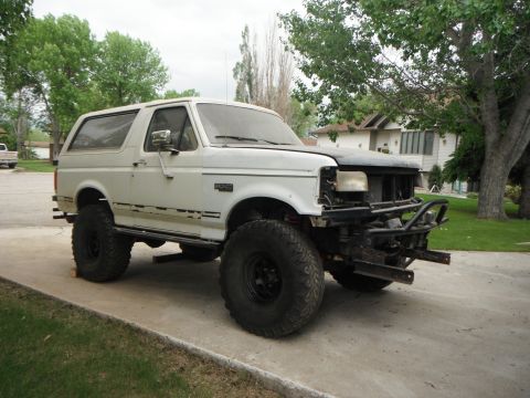 1990 Ford Bronco - This modified Ford Bronco sits on a driveway with a house and trees in the background.