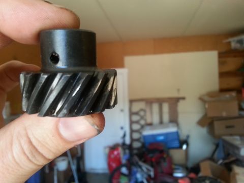 1981 Ford Bronco - A close-up of a metal gear, likely a replacement part, held in a person's hand in a cluttered garage setting.