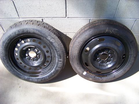 1999 Mercury Grand Marquis - Two spare tires and rims are displayed against a brick wall, with visible tire branding.