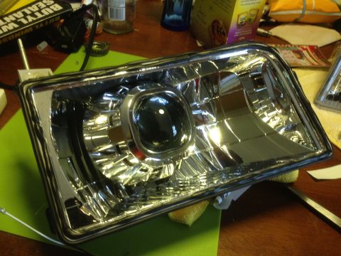 1992 Ford F-150 - A single headlight assembly with a projector lens is shown on a table, with various items in the background.
