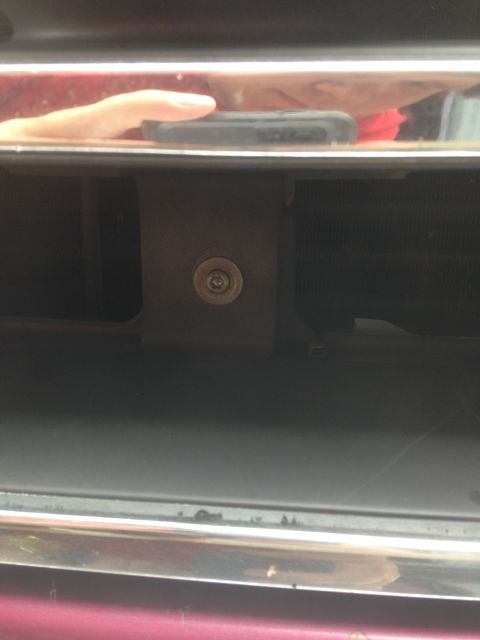 1992 Ford F-150 - A close-up shot focuses on a bolt and the grille of a vehicle, with a hand holding a phone reflected in the chrome trim.