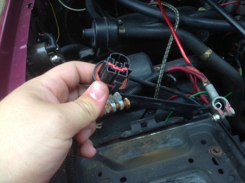 1992 Ford F-150 - A person is holding a wiring harness connector in the engine compartment of a vehicle.