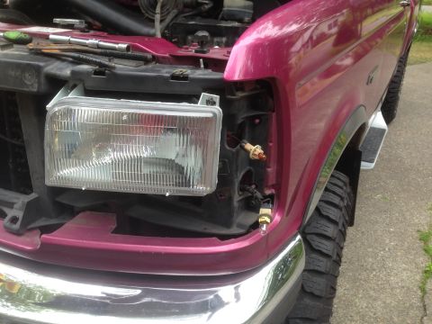 1992 Ford F-150 - The headlight assembly is removed from the front fender of a pink Ford F-150, with tools laid out on the fender.