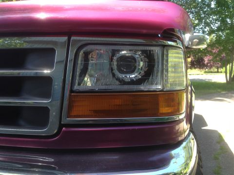 1992 Ford F-150 - Close-up of the front end of a red truck, highlighting its projector headlights and chrome grille.