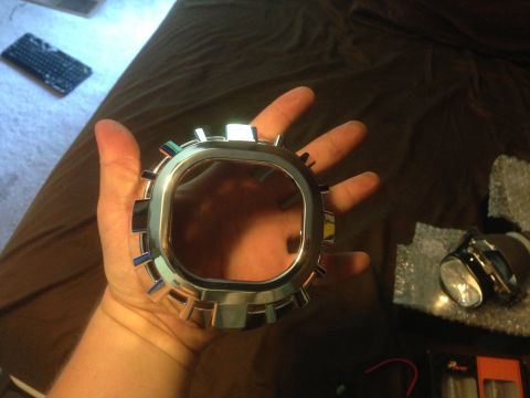 1992 Ford F-150 - A chrome bezel with gear-like protrusions is held in a hand, with a projector headlight visible in packaging.