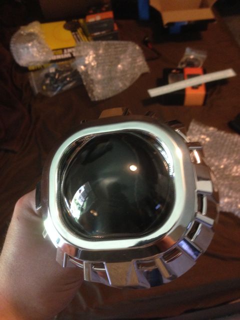1992 Ford F-150 - A person holds a chrome-trimmed headlight projector lens with various automotive parts in the background.
