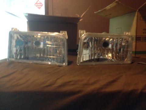 1992 Ford F-150 - Two clear plastic headlights are displayed on a brown surface, possibly for sale or installation.