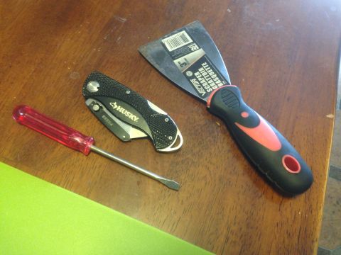 1992 Ford F-150 - A collection of tools, including a screwdriver, a Husky folding knife, and a Vector scraper, are laid out on a wooden surface.
