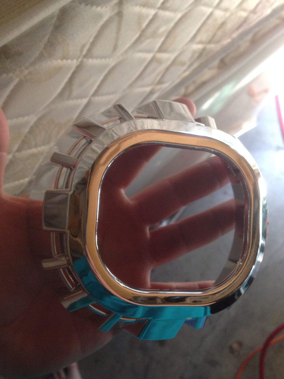 Chrome trim piece with a rectangular opening and metallic fins, held in a hand
