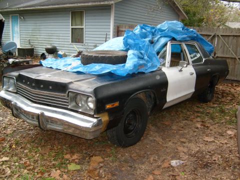 1974 Dodge Monaco - This 1974 Dodge Monaco police car is partially covered by a blue tarp and has a spare tire on its hood.