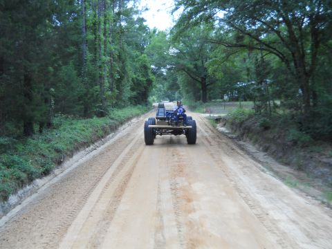 1992 Ford Bronco - A person drives a custom buggy down a dirt road surrounded by trees.