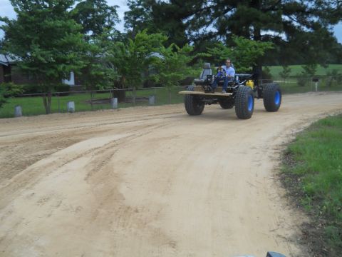 1992 Ford Bronco - A custom-built vehicle with large tires and a wooden platform is driven on a dirt road.