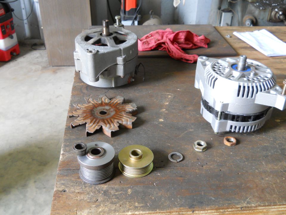 Two alternators, a rusty fan, two pulleys, and nuts on a workbench