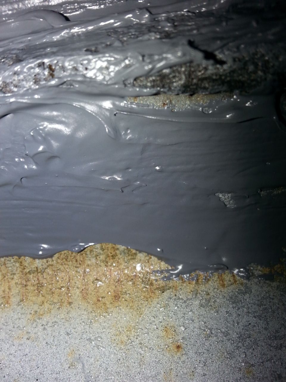Grey sealant applied to corroded metal surface with visible rust