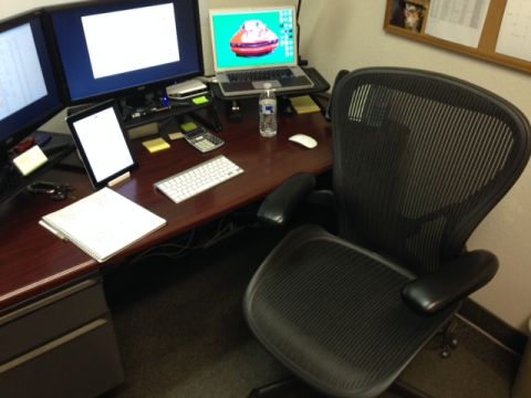 1987 Suzuki Samurai - A cluttered office desk features computers, a calculator, and a chair, with a laptop screen showing a vehicle.