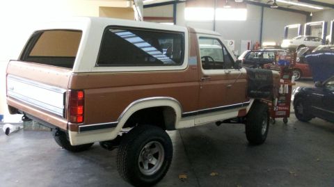 1982 Ford Bronco - Side view of a Ford Bronco in a workshop environment with other cars present.