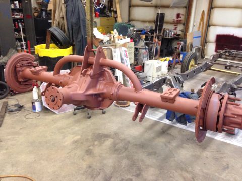 1993 Ford Bronco - A red-painted rear axle assembly is shown in a workshop setting, possibly undergoing restoration or repair.