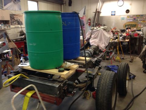 1993 Ford Bronco - A disassembled vehicle chassis sits in a workshop, topped with two large plastic barrels.