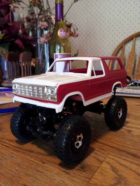 1995 Ford Bronco - A toy Ford Bronco model sits on a wooden table, with a bottle and flowers in the background.
