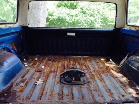 1979 Ford Bronco - The interior of a heavily rusted truck bed, showing a hitch mechanism and debris scattered across the floor.