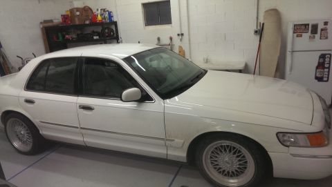 2000 Mercury Grand Marquis - A white sedan is parked inside a garage with shelves and a refrigerator in the background.