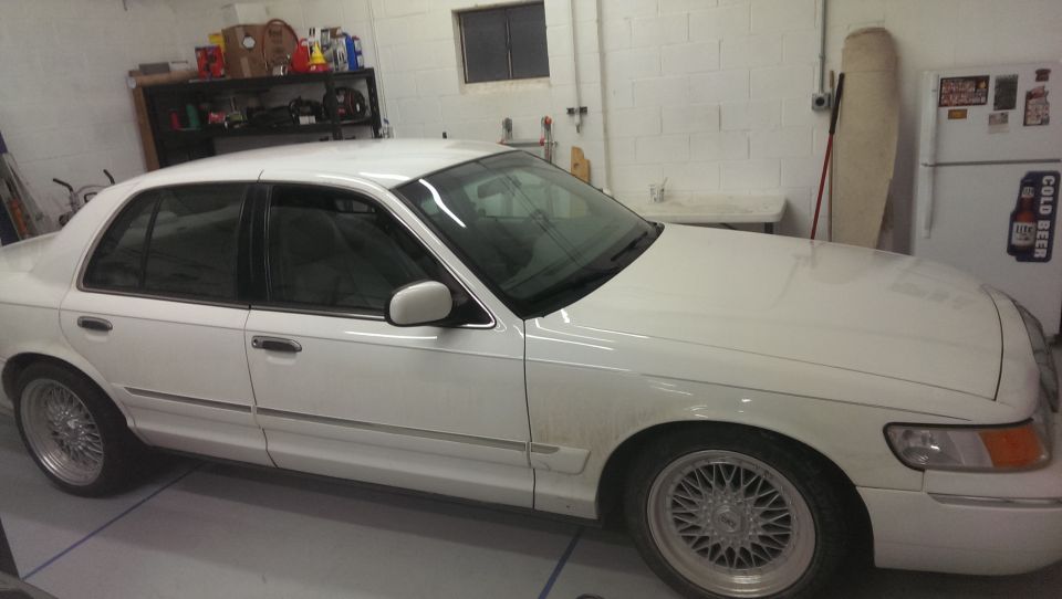 White sedan parked in a garage, side and front quarter view. Aftermarket wheels visible