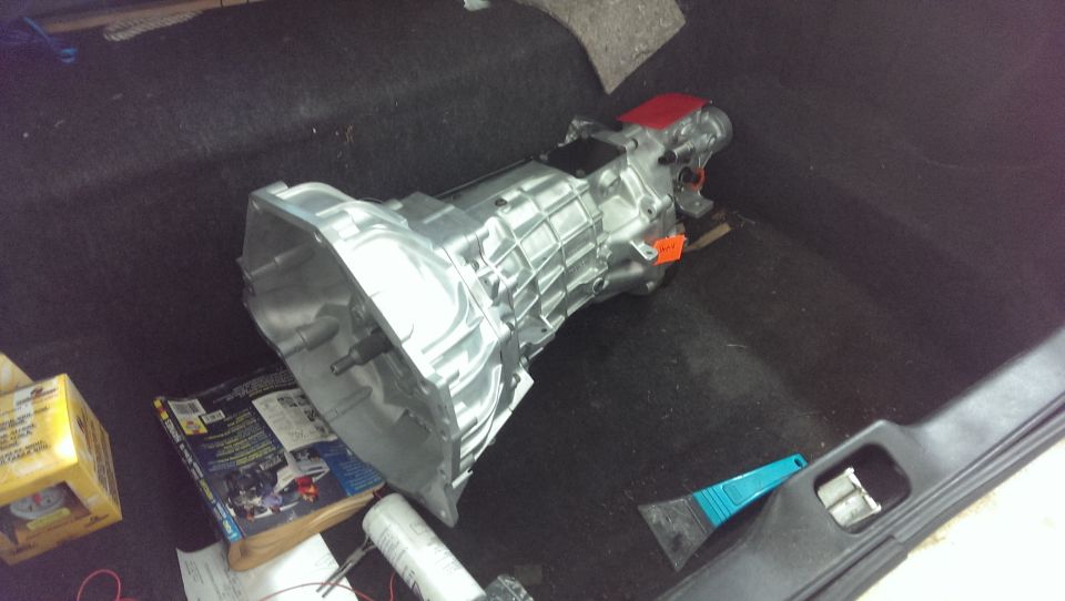 Manual transmission sitting on dark carpet with a yellow box and some papers