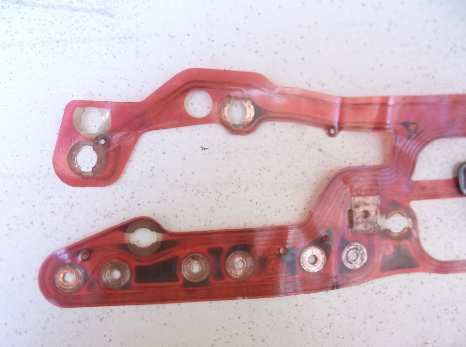 Close-up of a red circuit board with copper contacts, likely for a car's dashboard