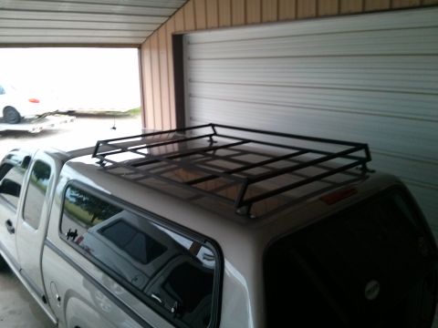 1986 Ford Bronco - A silver pickup truck is parked inside a garage, fitted with a black roof rack and a camper shell.