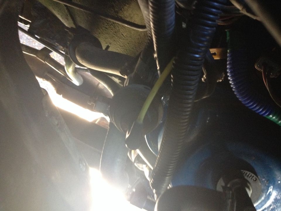 Underside view of vehicle with hoses, wires, and engine parts visible