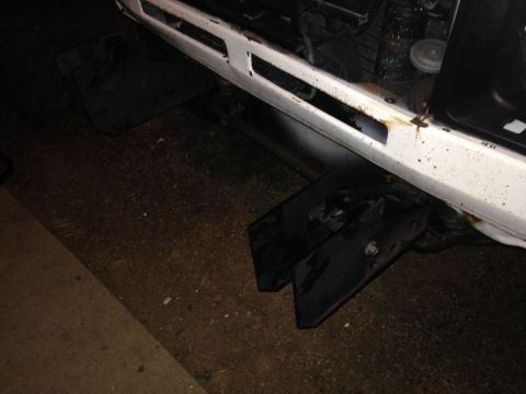 1990 Mitsubishi Montero - Close-up of a white vehicle's front bumper area, showing black tow hitch components and signs of wear.
