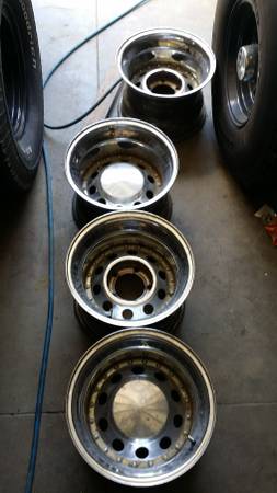 1978 Ford Bronco - A set of four chrome wheels and tires are lined up on a concrete surface, with a blue cord running along the floor.