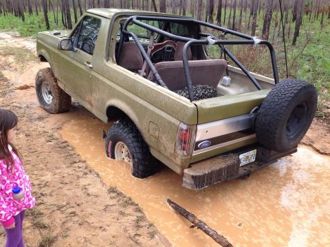 1994 Ford Bronco - This modified Ford Bronco is deep in the mud, with a roll cage and spare tire visible.