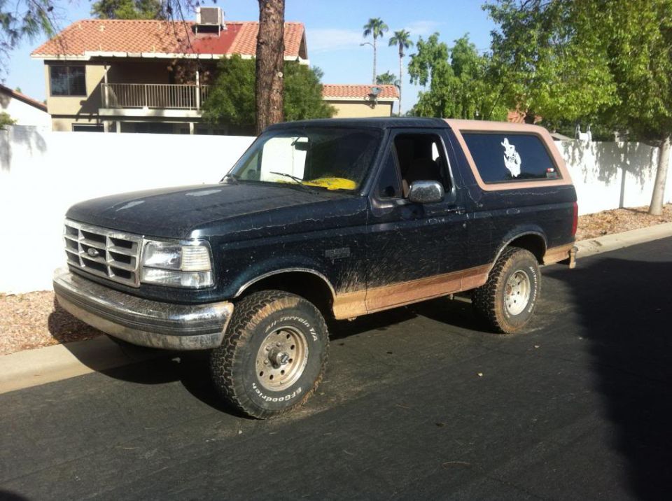Dark blue Ford Bronco with tan top, mud splattered on lower body panels