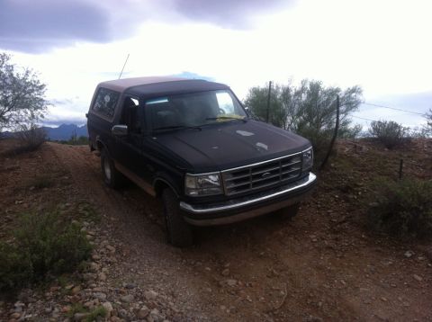 1994 Ford Bronco - A black Ford Bronco with a tan top drives on a dusty, rocky trail.
