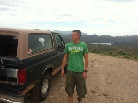 1994 Ford Bronco - A man stands next to a Ford Bronco on a dirt road with a scenic mountain and lake view in the background.