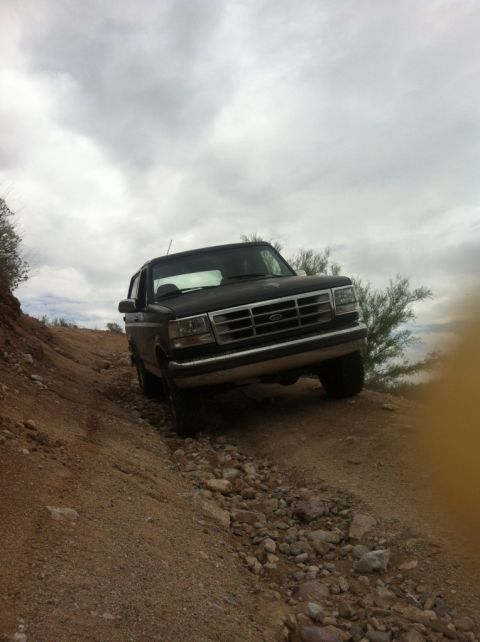 1994 Ford Bronco - This Ford Bronco is navigating a rough, off-road path with loose rocks and dirt.