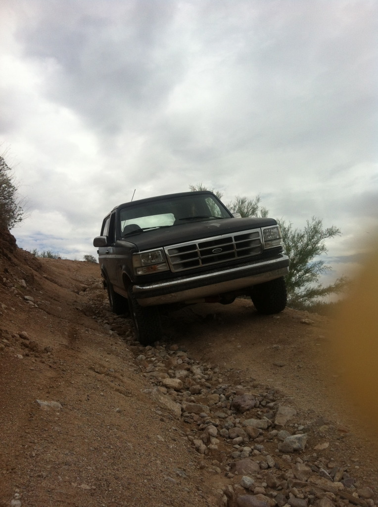 Black Ford Bronco driving on a rocky, dirt trail under a cloudy sky