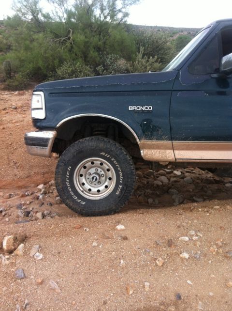 1994 Ford Bronco - A dark blue Ford Bronco with tan lower trim is seen from the front quarter angle on a dirt road.