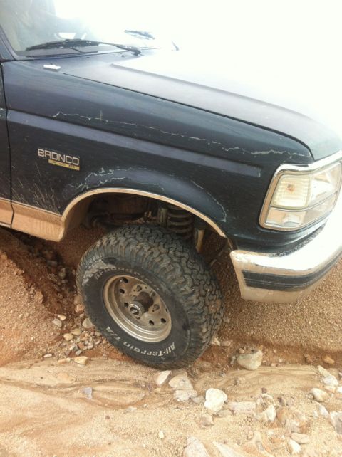 1994 Ford Bronco - A dark green Ford Bronco is shown from the front quarter, with its front tire in a ditch.
