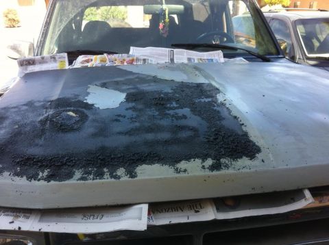 1994 Ford Bronco - The hood of a vehicle is covered in peeling paint, with newspapers laid out to catch debris.