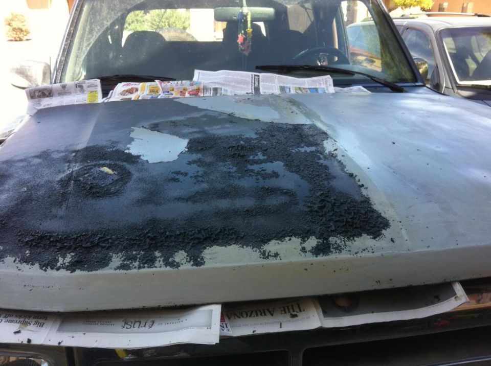 hood of a vehicle with old paint peeling off, newspapers underneath